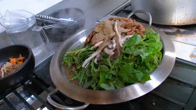 Hot pot dish made by pouring broth over fresh vegetables and mushrooms in a metal bowl