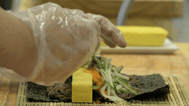 Chef preparing futomaki sushi with various ingredients