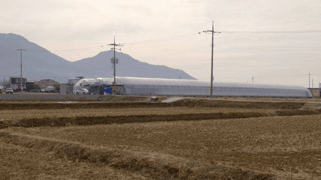 A rural farm with greenhouses and mountains