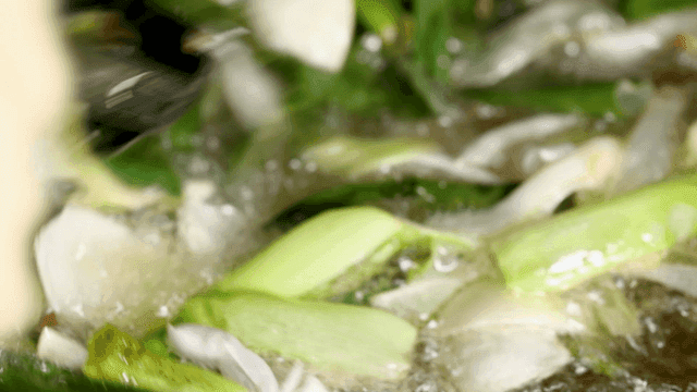 Green onions frying in hot oil, hands stirring