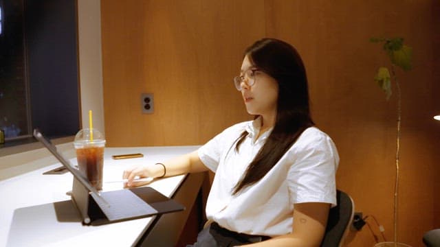 Woman working on a laptop with iced coffee