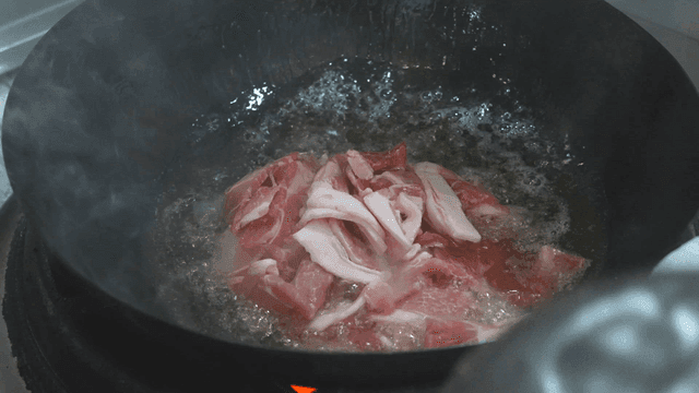 Raw pork slices poured into hot wok oil