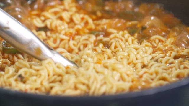 냄비 속에서 집게로 저으며 끓이고 있는 맛있는 라면