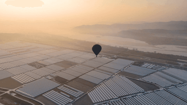 Hot air balloon in air above field with greenhouses