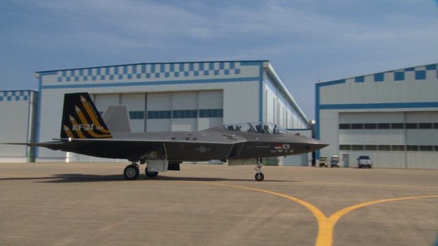 Jet fighter taxiing on airport runway near hangars