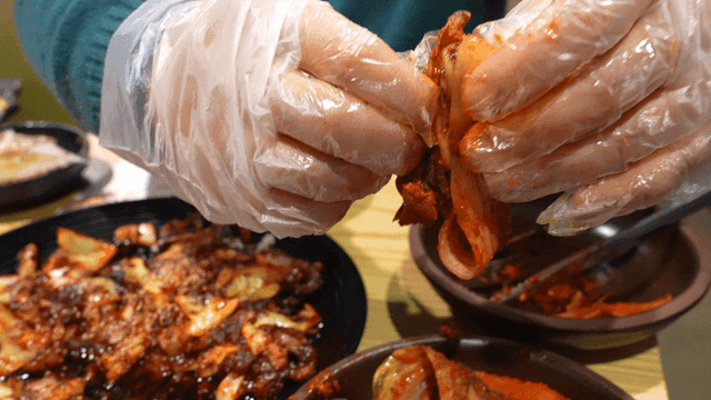 Person eating kimchi with gloved hands