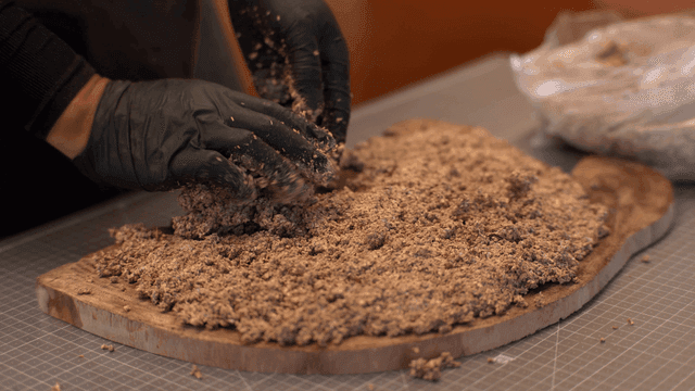 Hand applying sawdust and glue mixture onto wooden piece