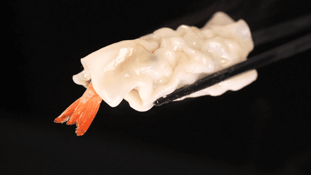 Chopsticks picking up shrimp dumpling placed in steamer