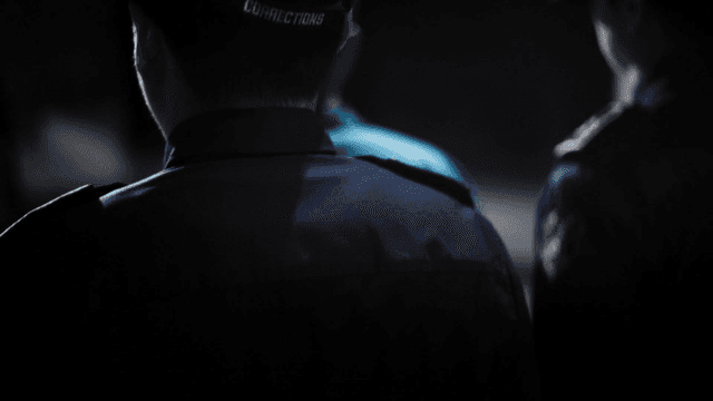 Guard escorting person through dark hallway