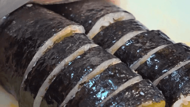 Gimbap being sliced on a cutting board