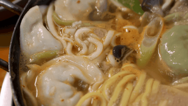 Dumpling hot pot broth with boiling dumplings and noodles