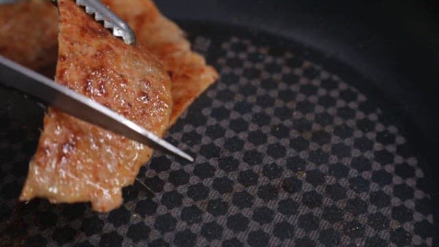 Grilled meat being sliced with tongs and scissors