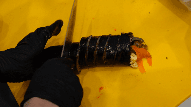 Gimbap being sliced on a yellow cutting board