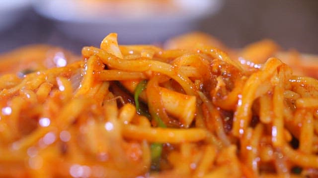 Chopstickful of spicy stir-fried jjambbong with steam rising from the pot