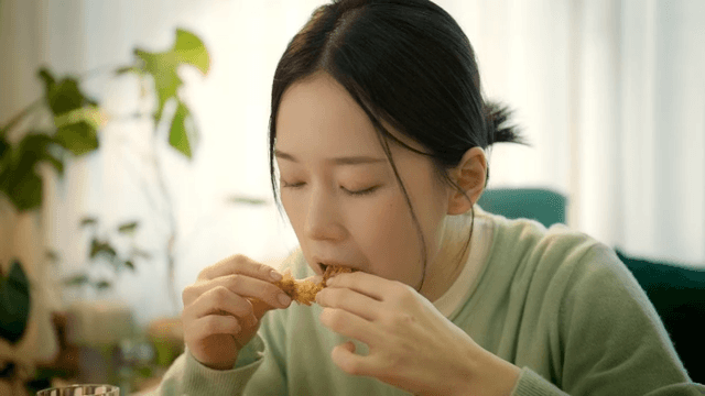 Woman eating chicken and drinking beverage at home