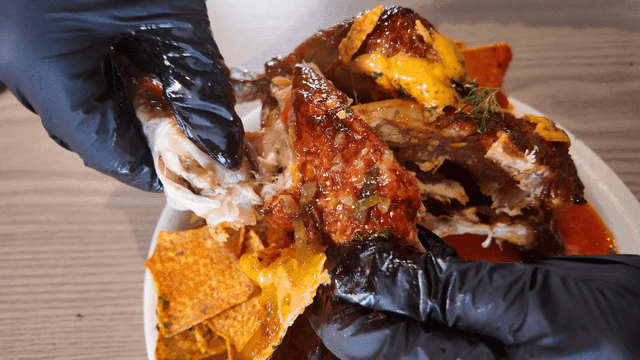 Hand tearing apart whole chicken with cheese and chips