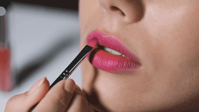 Woman applying pink lipstick with brush