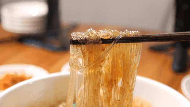 Chopsticks picking up Suanlafen in spicy broth