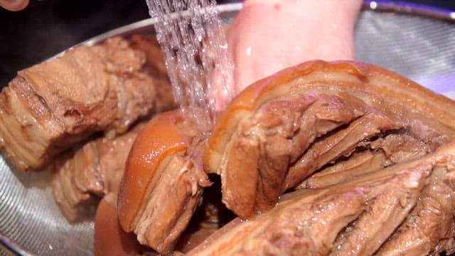 Boiled pork slices being rinsed under water