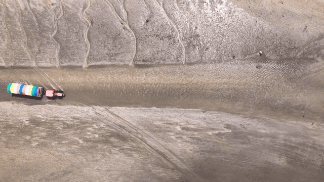 Tractor passing along coast flowing through mudflats