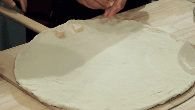 피자 도우 위에 치즈 큐브를 올리는 손