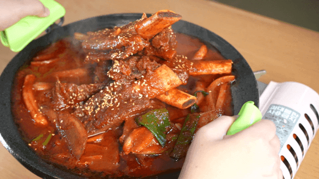 Spicy braised short ribs being transferred to gas stove