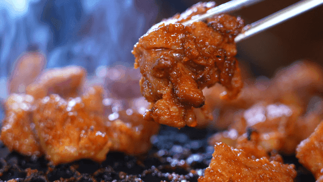 Chopsticks picking up marinated meat grilled at barbecue