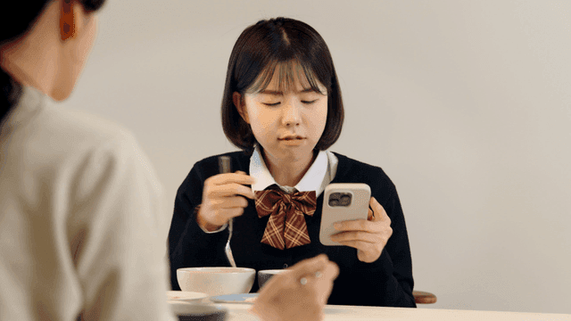 Mother nags her daughter while she eats while looking at her phone.