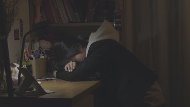 어두운 방에서 책상에 엎드려 잠든 학생
