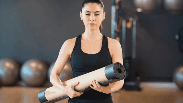 체육관에서 요가 매트를 들고 있는 여성