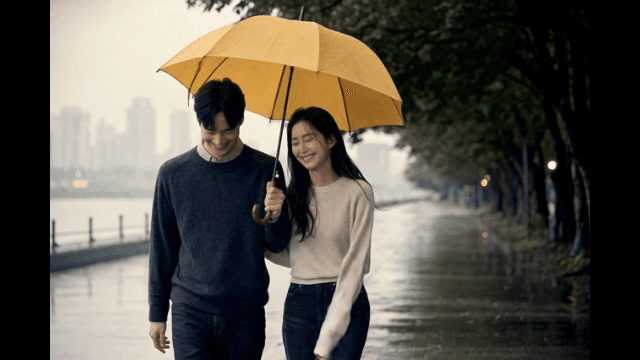 Couple walking along riverside promenade with umbrellas on rainy day