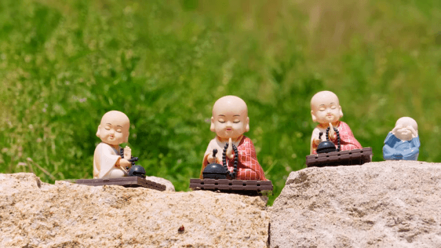 녹색 배경의 돌 위 작은 승려 조각상