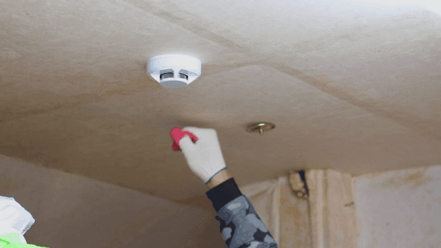 천장에 연기 감지기를 설치하는 사람