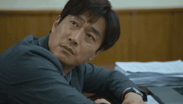 서류와 노트북이 있는 책상에 기대어 쉬는 남자 직장인