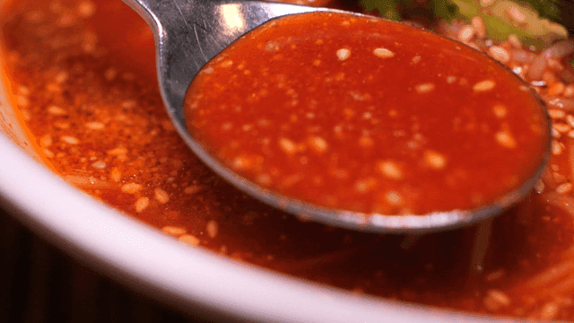 Spoon scooping up spicy bibim guksu broth