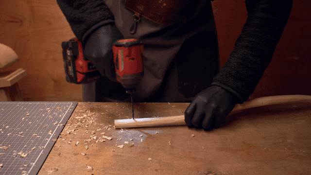 테이블 위에서 나무 조각을 드릴로 작업하는 사람