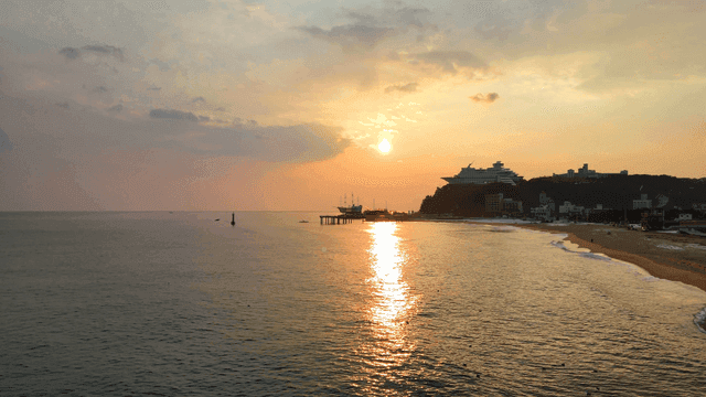 Sunset on tranquil beach with boat-shaped resort visible in distance