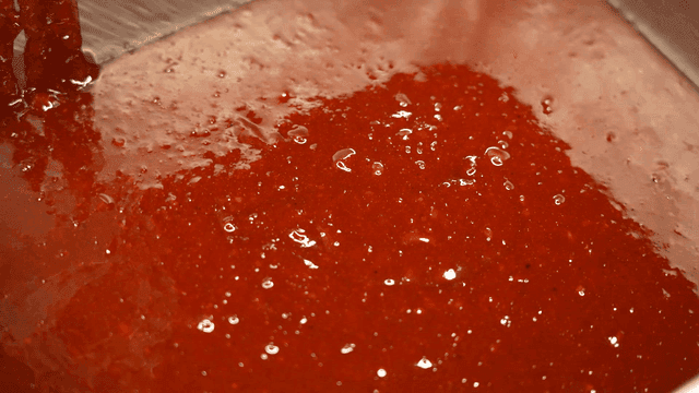 Thick red sauce being poured into a container