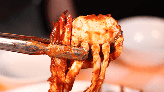 Spicy crab and seafood stew lifted with tongs