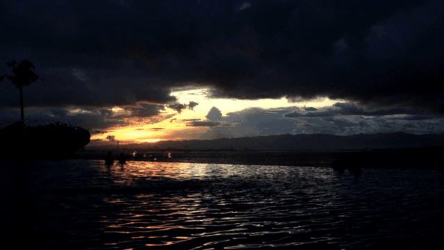 Sunset over calm sea and silhouettes of people swimming