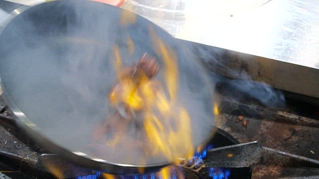 Flames rising from a pan with beef cooking