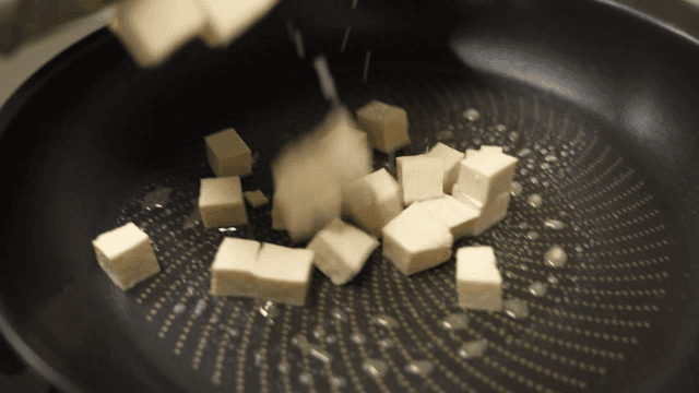 Tofu cubes poured from cutting board into frying pan