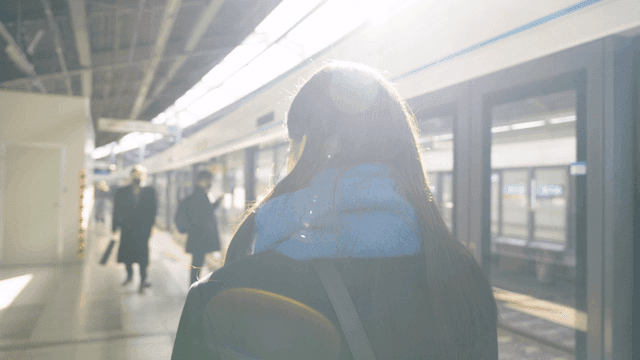 Back of a woman moving through a sunlit subway station