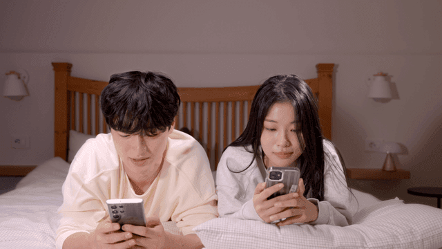 Couple using smartphones side by side on bed