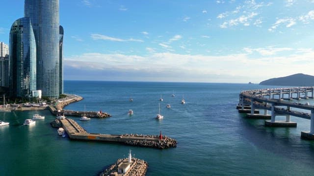 Boats heading out to sea between long bridge and buildings