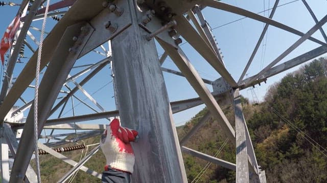 Worker holding bolts and climbing up transmission tower to inspect it