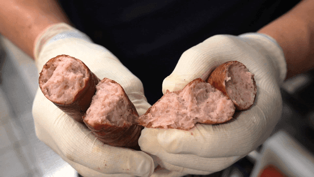 Gloved hand slicing sausage