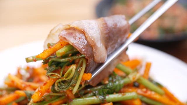 Slices of pork belly being picked up with chopsticks alongside parsley salad