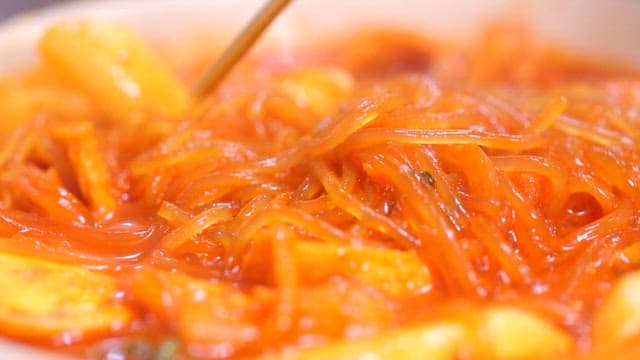 Chopsticks holding glass noodles of spicy tteokbokki