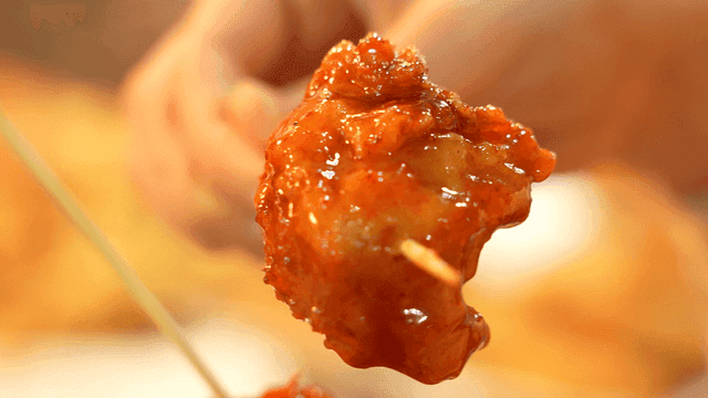 A hand holding a skewer of glazed chicken